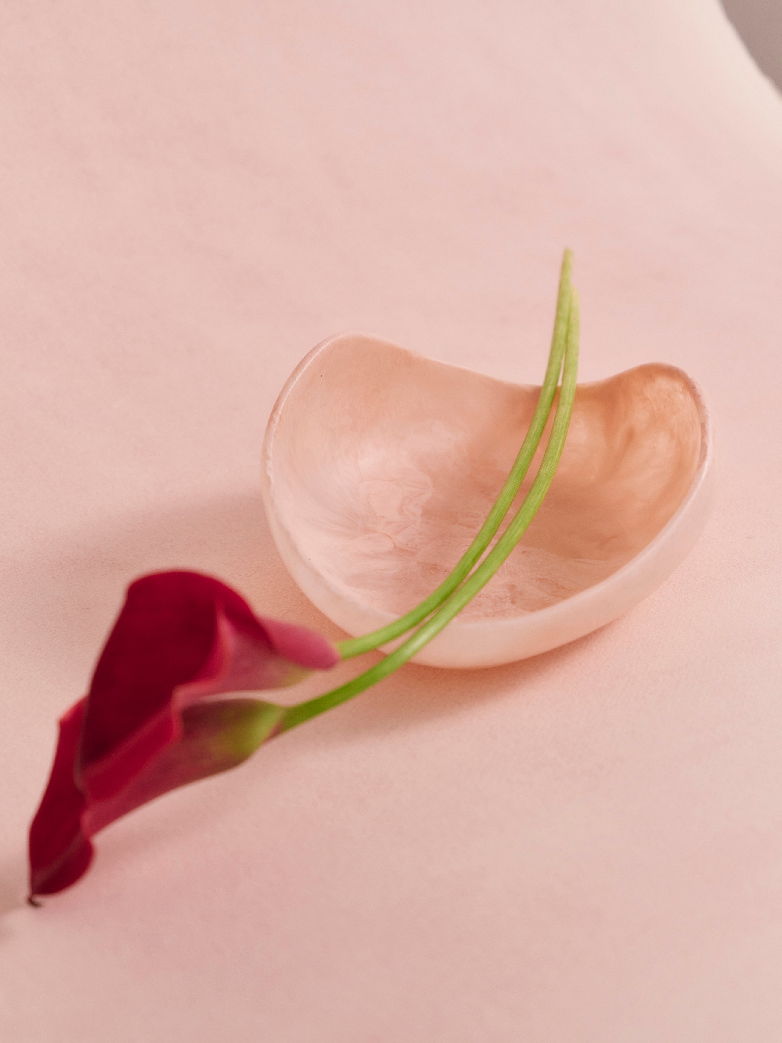 Pink sculptural resin bowl with a floral stem laid across it