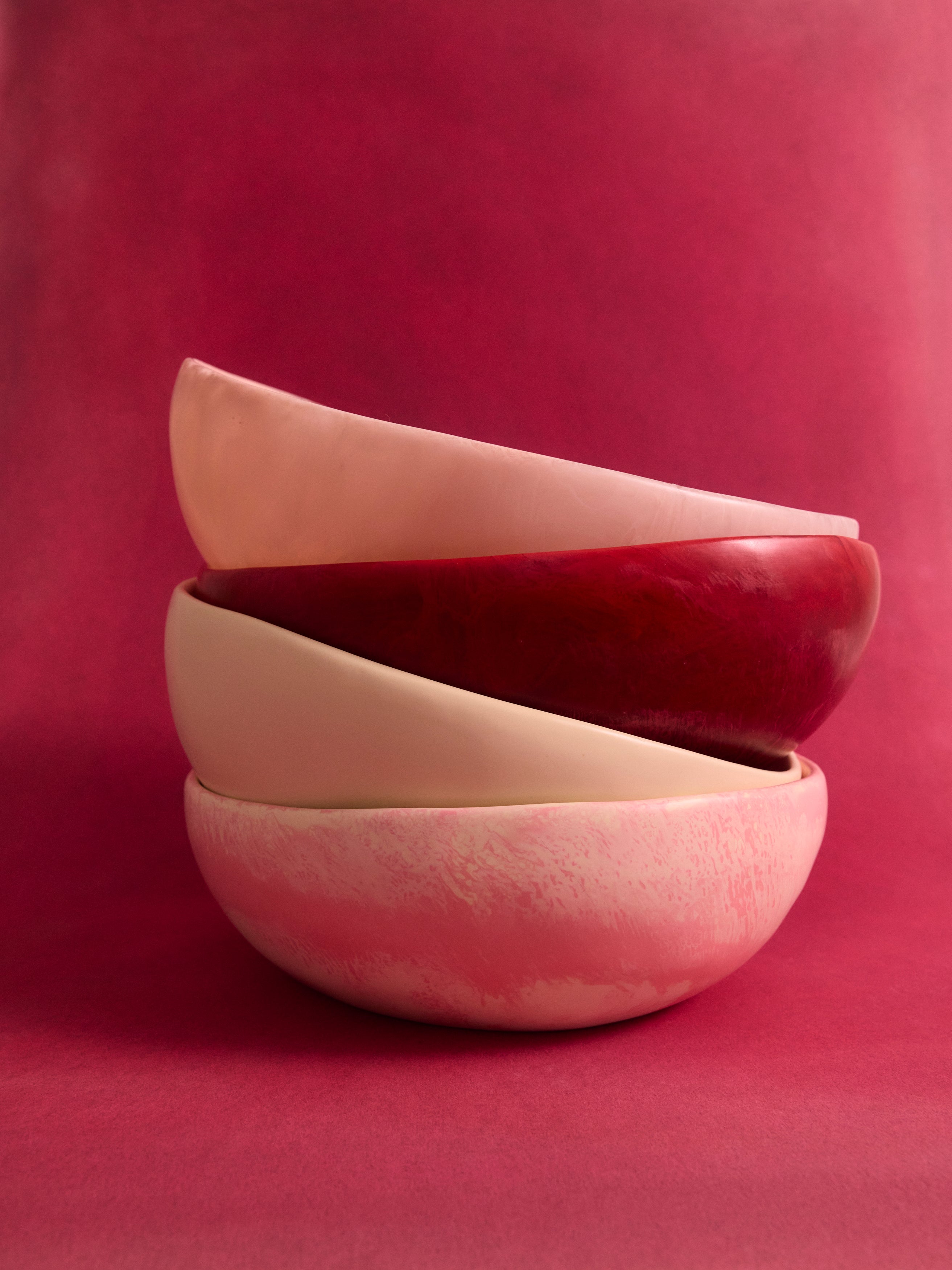 Stack of resin salad bowls in pinks and cream on a pink backdrop