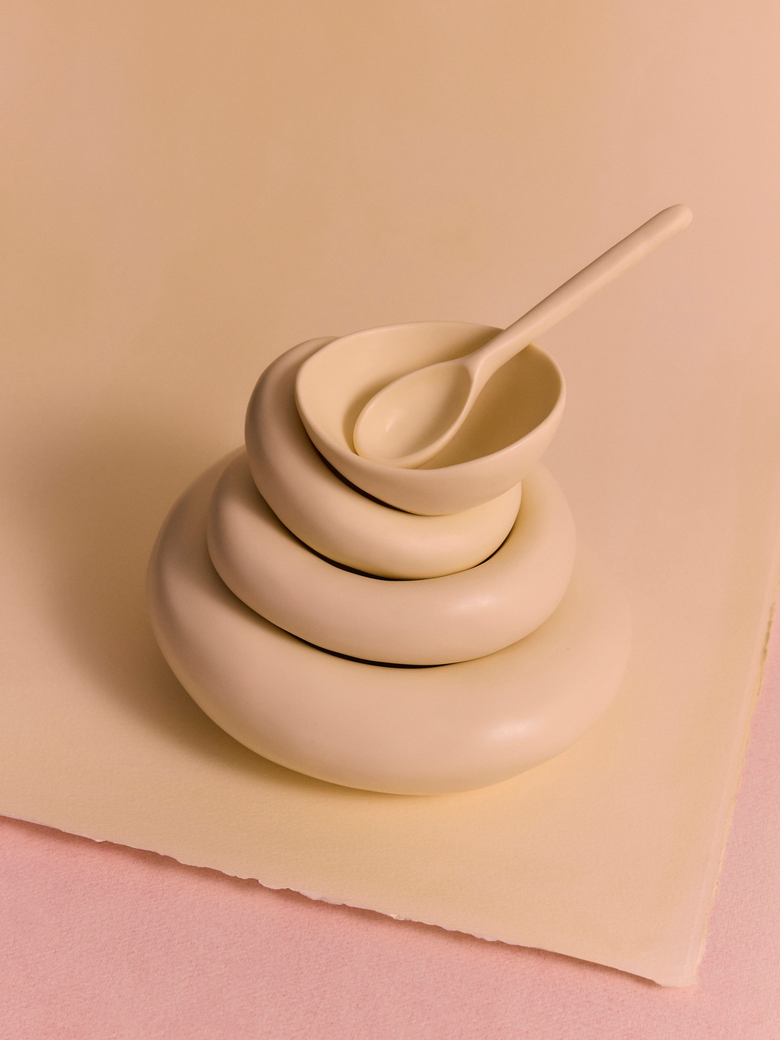 Stack of cream-coloured resin bowls with a spoon on a beige background