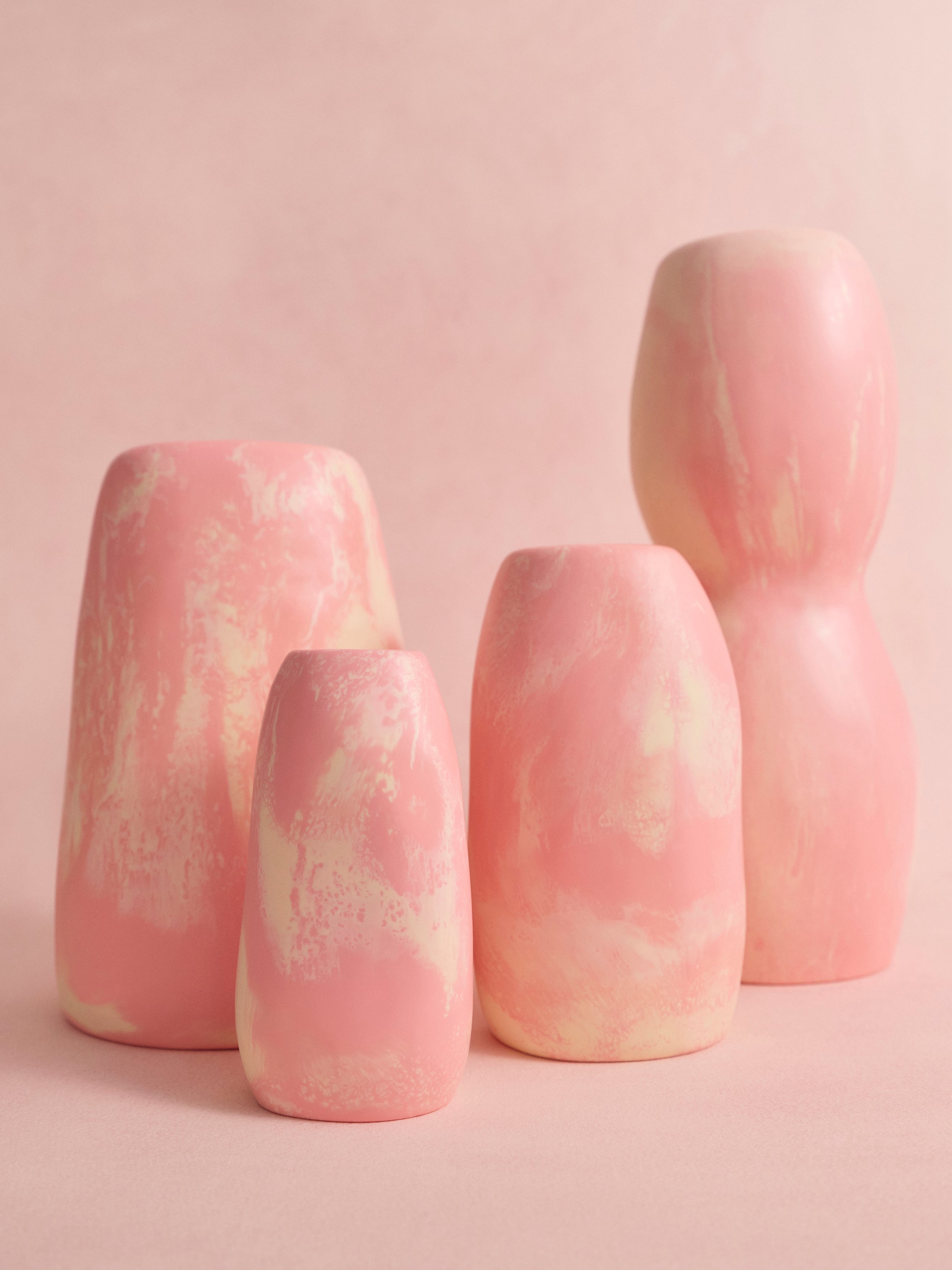 Set of four pink and cream marbled resin vases in a variety of organic shapes on a pink background