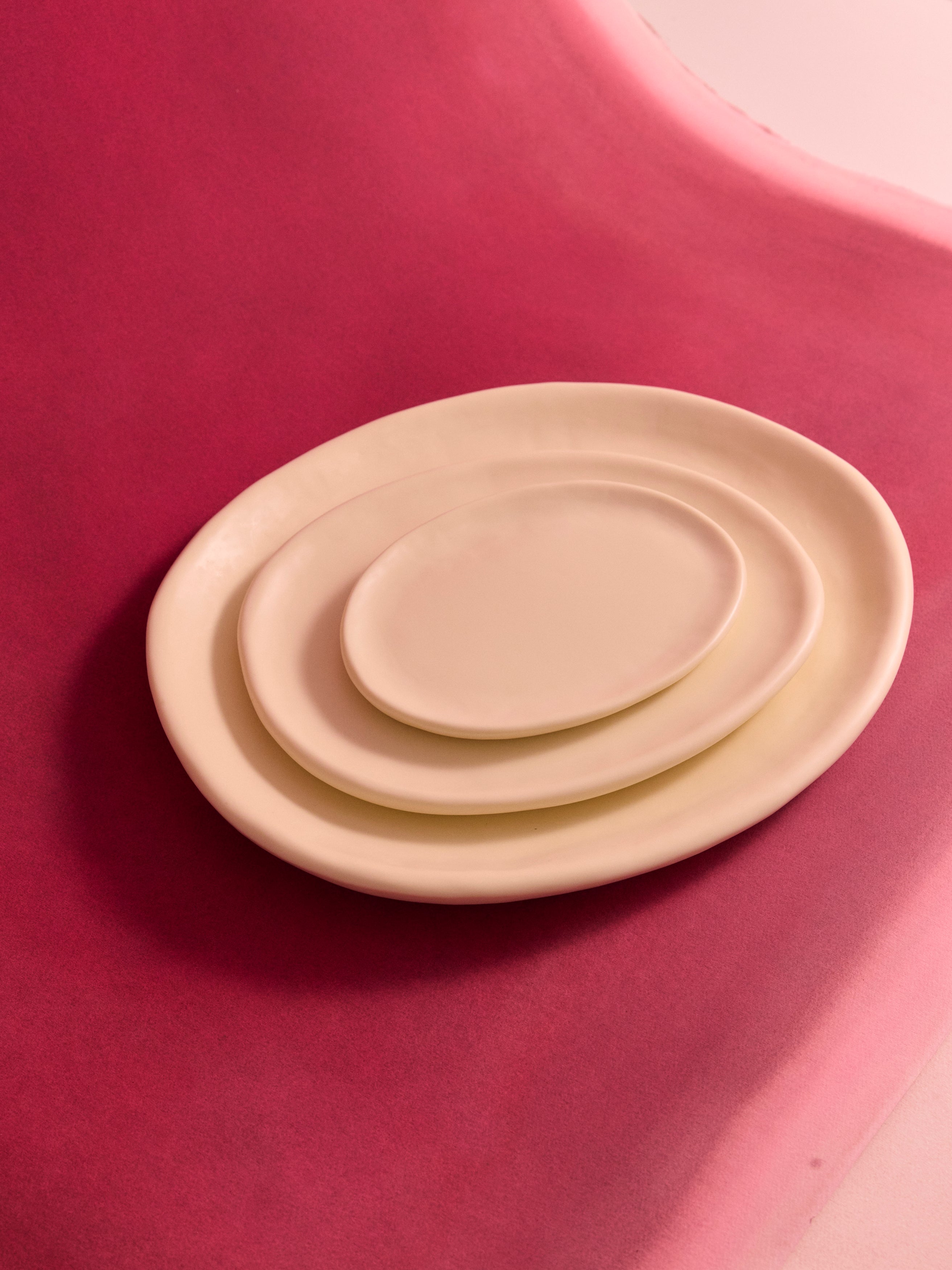 Stacked cream coloured resin serving plates on a deep pink backdrop