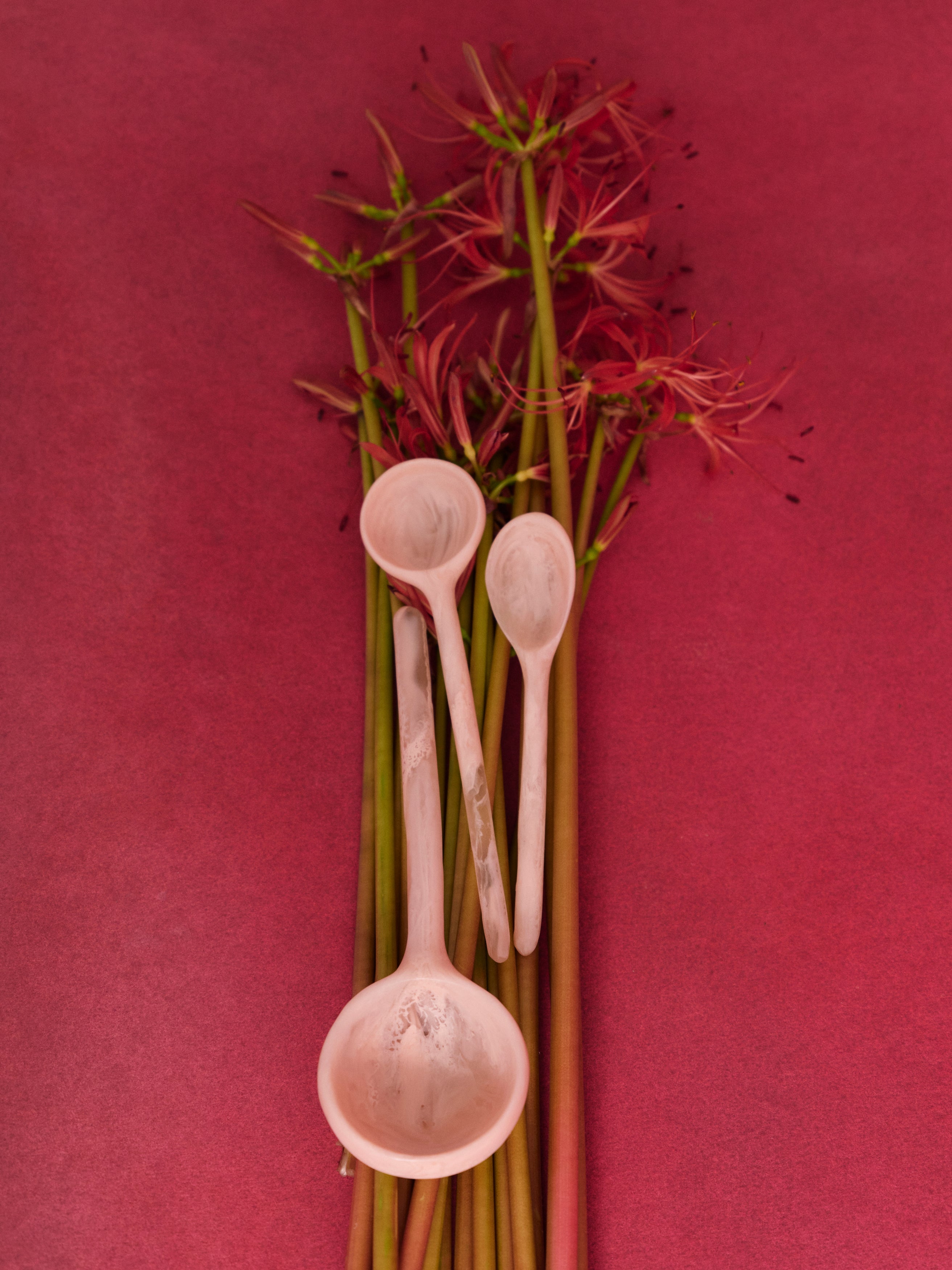 Three pink resin spoons laid upon a bunch of red flowers