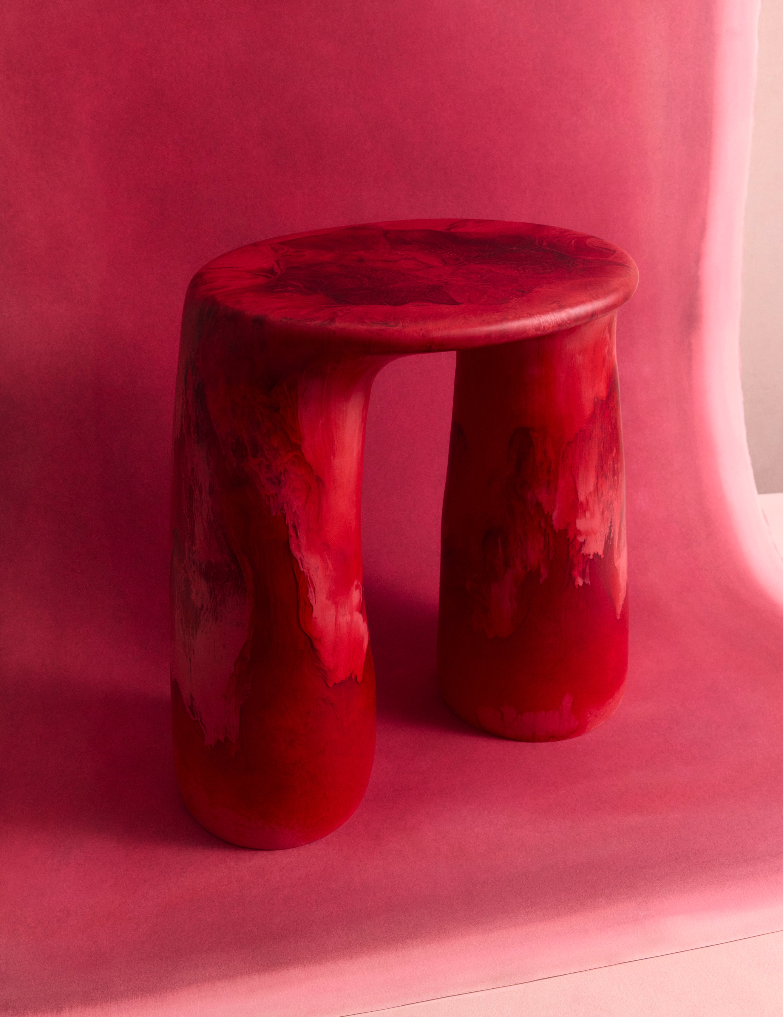Deep red two legged table on a pink backdrop