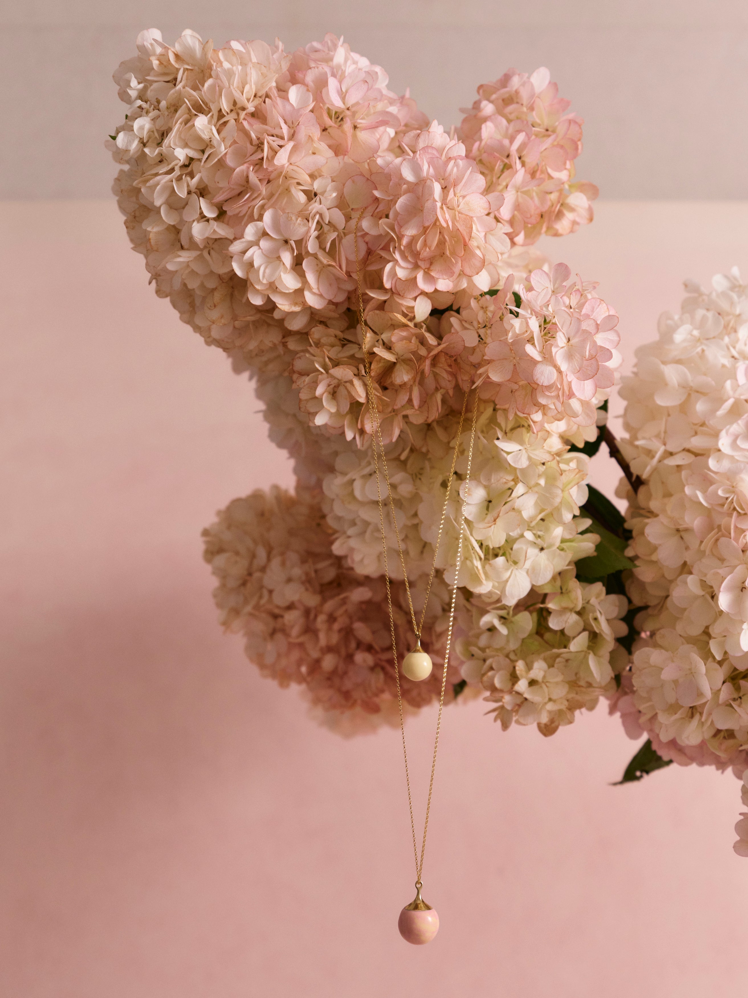 Pink and cream resin ball pendant draped from pink floral arrangement on a pink backdrop