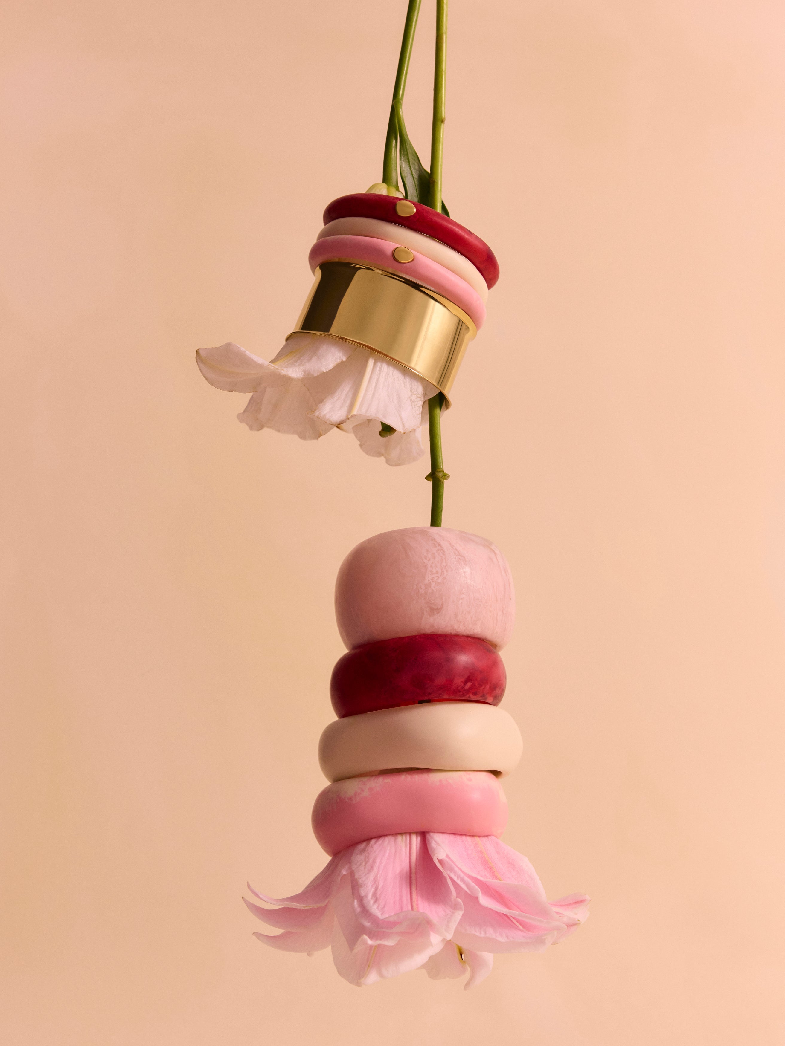 Lillies with pink, cream, and brass bangles stacked on their stems, on a beige backdrop
