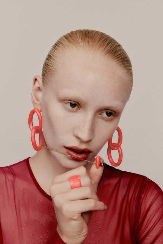 Model with red stud drop earrings, red large resin ring and fine gold toned necklace with red resin detail