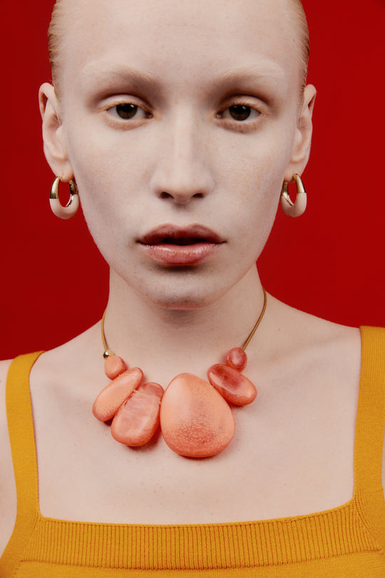 Model with orange choker necklace on leather cord with small brass detail and pink toned with brass detail hoop earrings