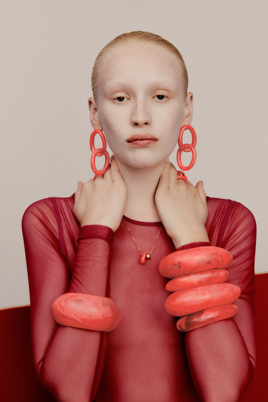 Model with orange toned bangles and stud drop earrings, gold toned necklace with resin detail