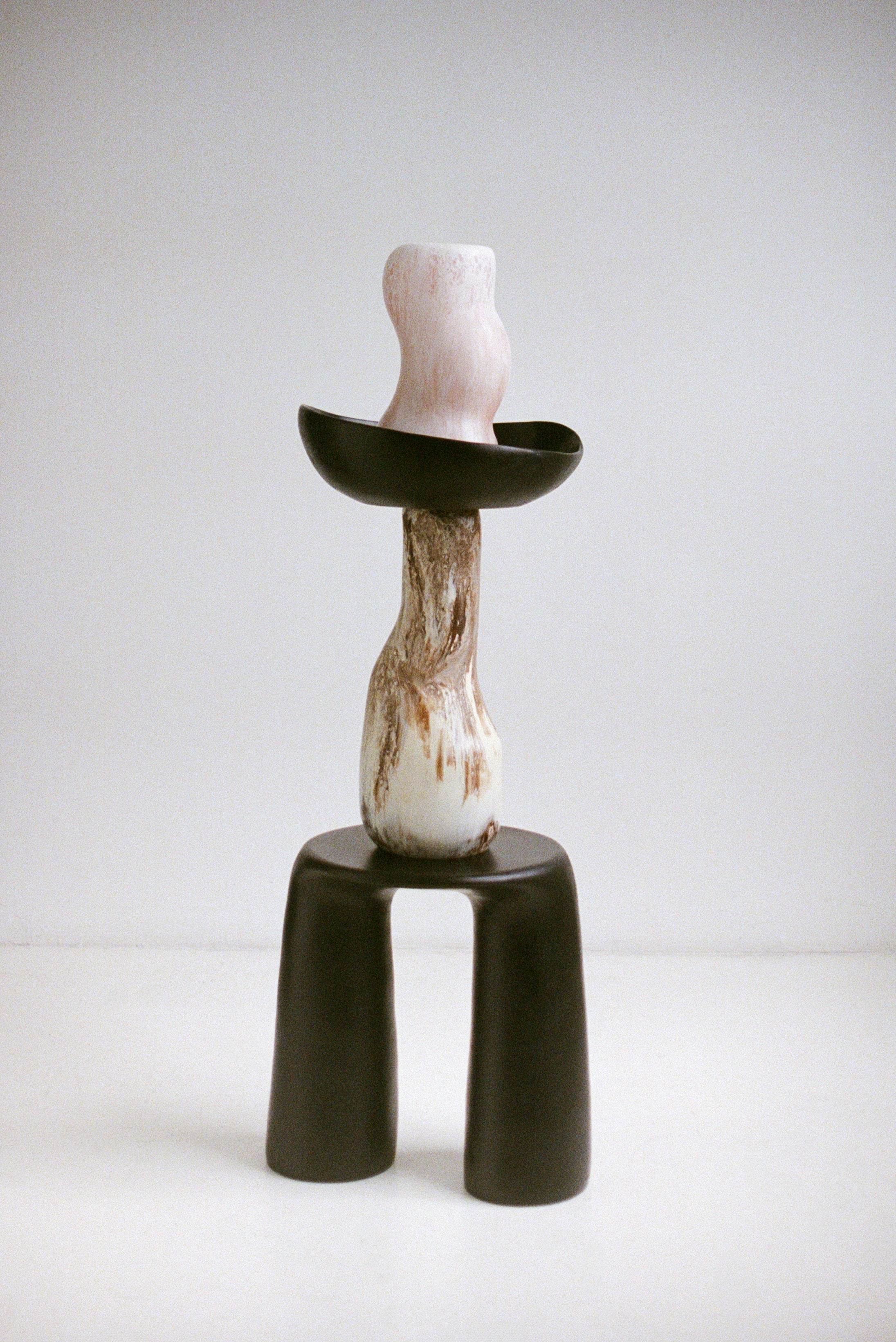 Handmade two legged black table with tall brown vase, large black bowl and white curved vase upon
